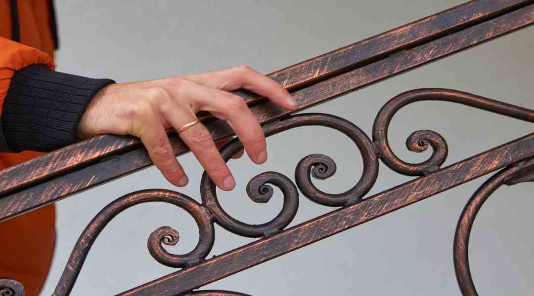 A homeowner walking up their staircase inside their house while holding onto a luxurious metal hand railing.