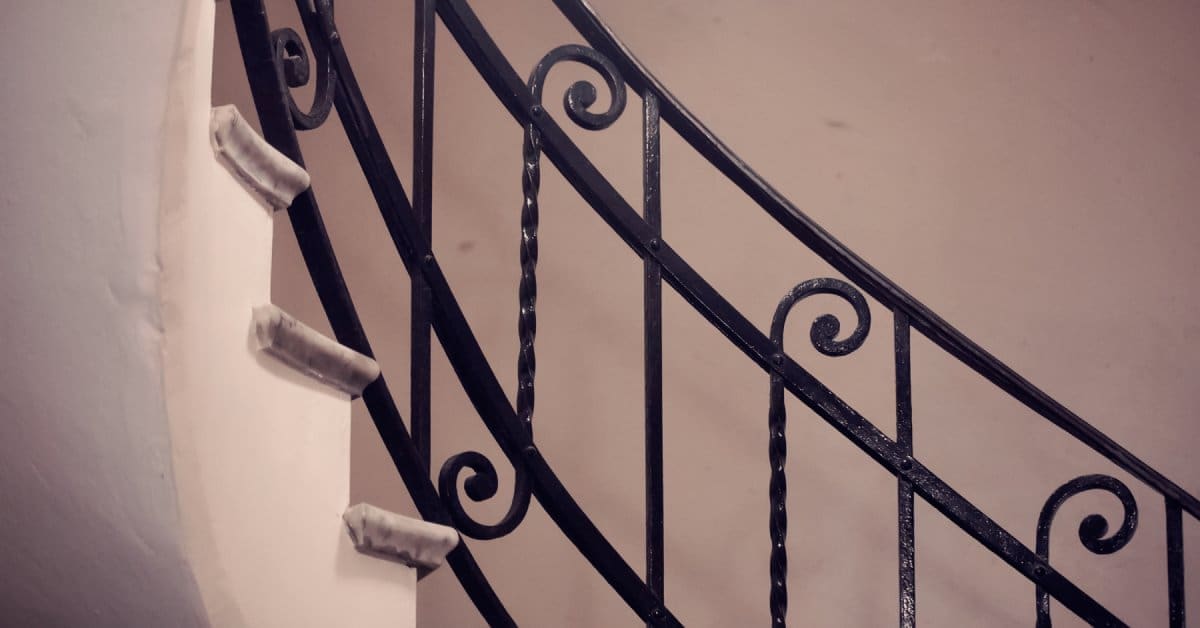 A black metallic handrail installed to a curved staircase. There is a spiral design on the side of the railing.