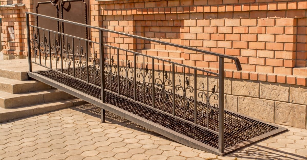 An exterior handrail installed onto a metallic ramp. The ramp is attached to a staircase outside of a home.