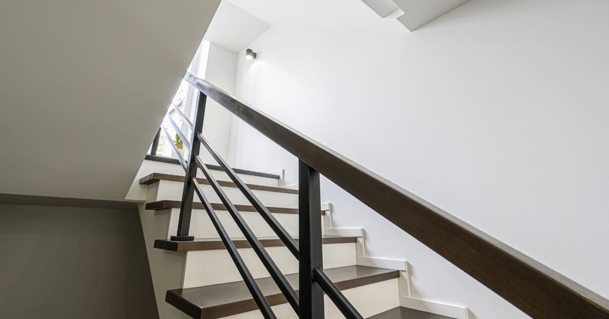 A staircase with wood steps and white risers. The black metal handrail has clean lines and square edges.