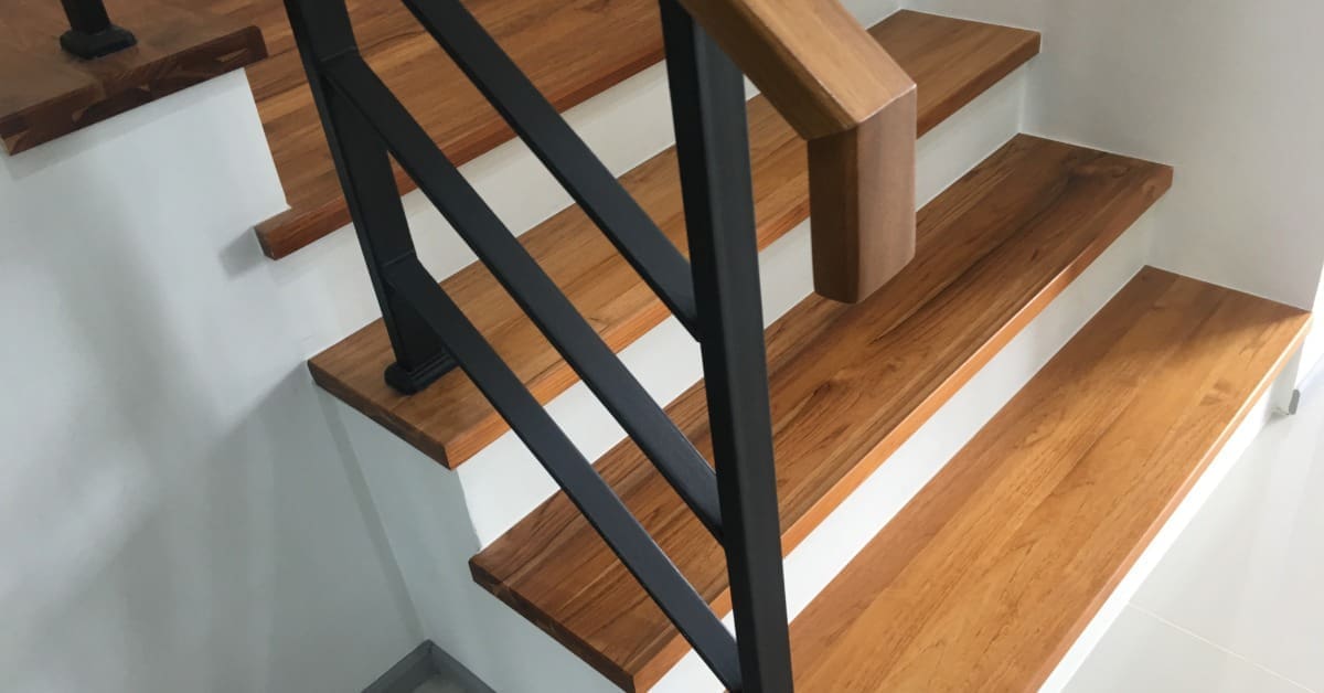 A close-up of a wooden steps with white risers, a black metal railing with horizontal posts, and a wooden handrail.